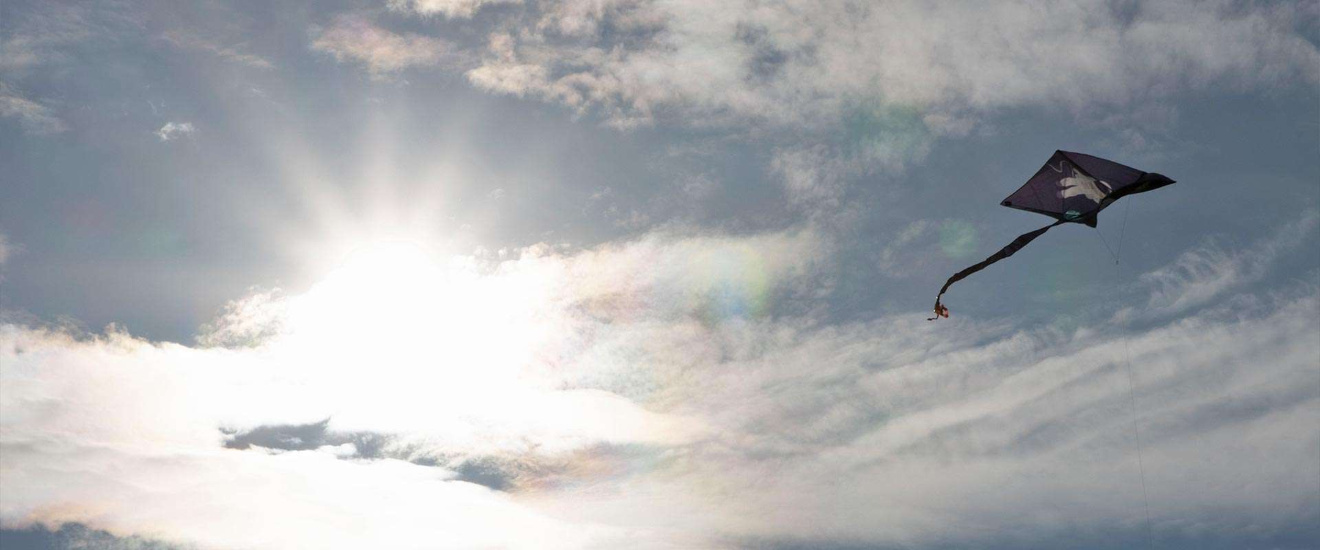Ein Flug-Drache und die Sonne stehen am leicht bewölkten Himmel.